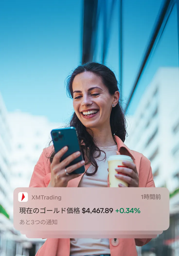 Woman outdoors looking at her phone, reading an XMTrading notification showing gold price rising