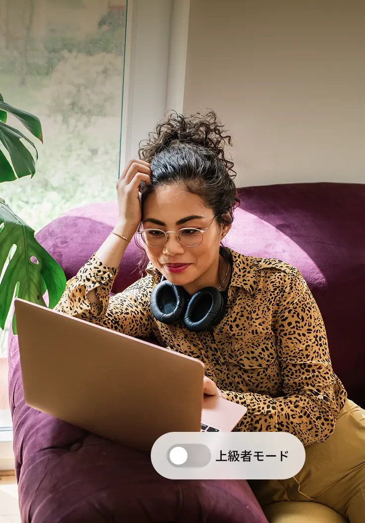 Woman sitting on a sofa with a laptop, focused on her screen next to a toggle labeled ‘Advanced Mode.