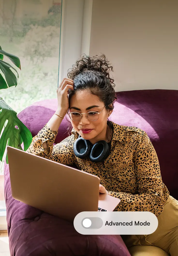 Woman sitting on a sofa with a laptop, focused on her screen next to a toggle labeled ‘Advanced Mode.