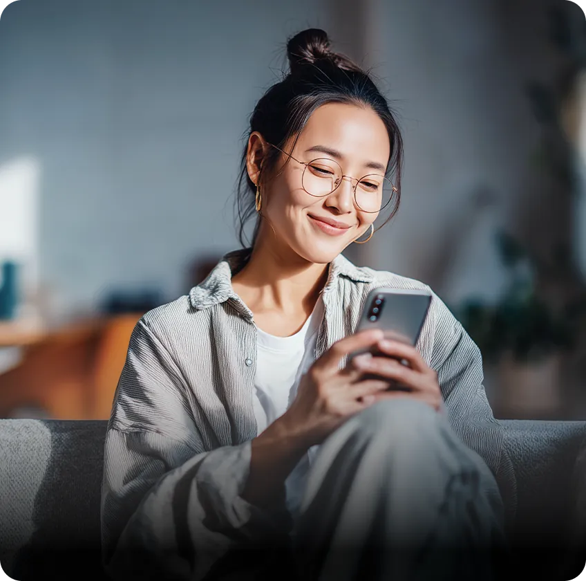 Young woman with glasses looking at her phone and smiling.