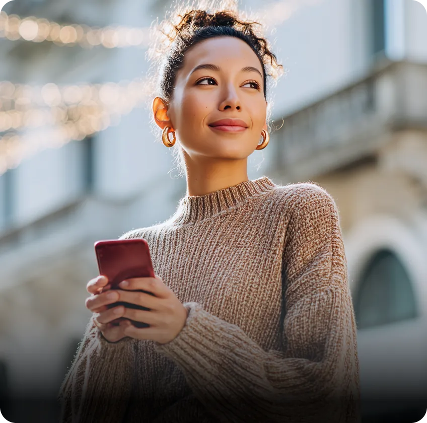Woman holding smartphone outdoors in warm sunlight.